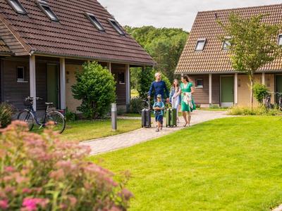 Una familia con dos niños camina entre casas de vacaciones sobre césped cuidado.
