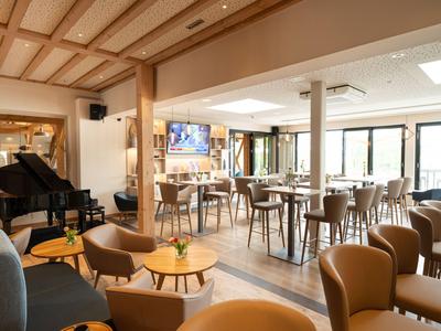 Moderner, heller Hotel-Loungebereich mit Stühlen, Tischen und einem Flügel in warmem Holzdesign.