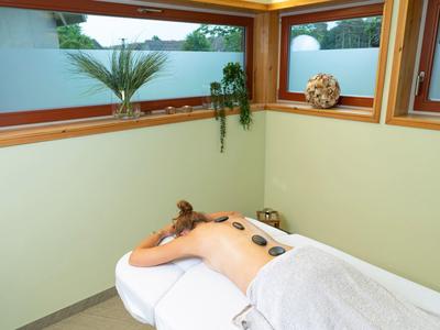 Persona acostada relajada con piedras calientes en la espalda en una sala de bienestar tranquila.