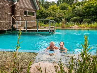 Zwei Personen genießen ein Bad im klaren Außenpool vor einem modernen Holzhaus.