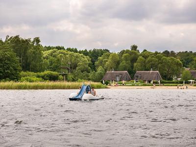 Lago con pedalón y dos casas en la orilla boscosa bajo cielo nublado.