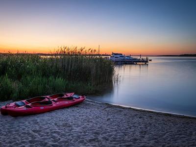 Lago tranquilo con botes en la orilla al atardecer y un kayak rojo en la playa de arena.