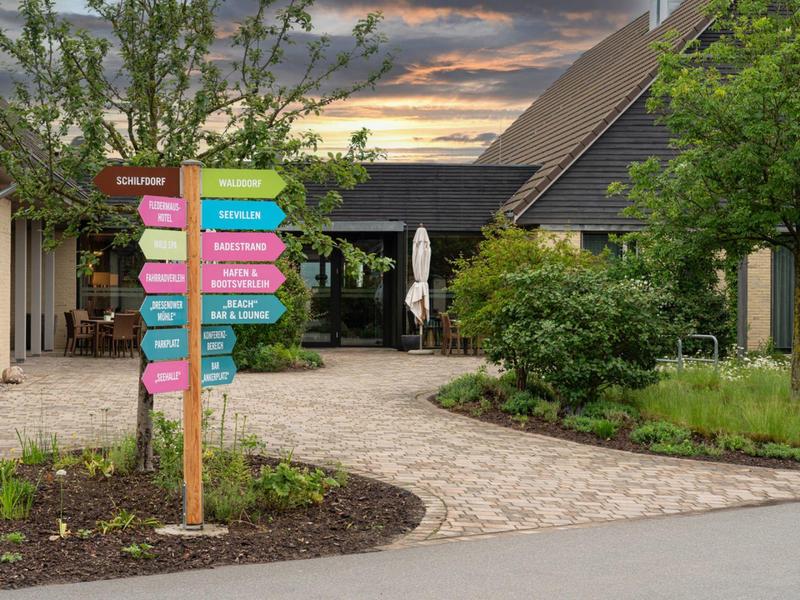 Señal con carteles coloridos en un jardín de hotel cuidado al atardecer.