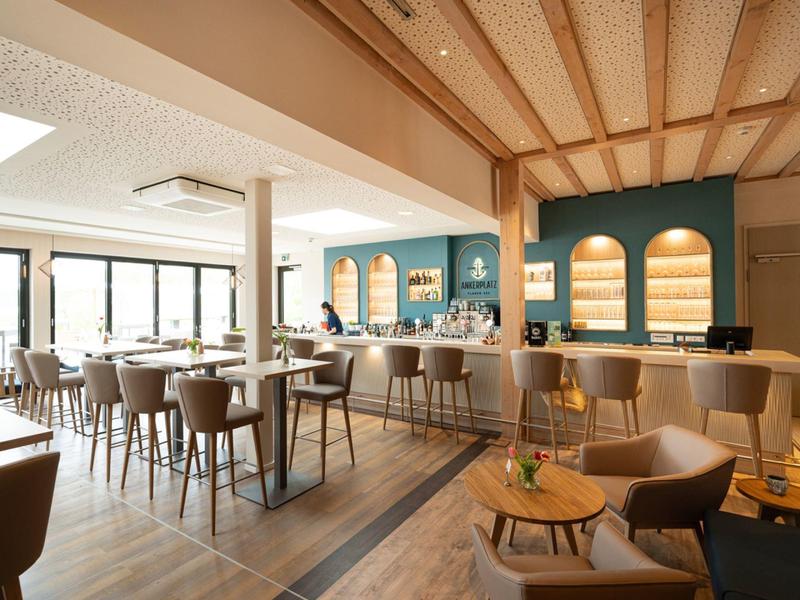 Restaurante de hotel luminoso con vigas de madera, mesas modernas, sillas y una barra con mostrador.