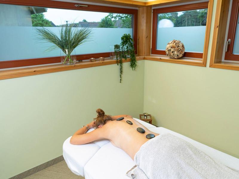 Persona acostada relajada con piedras calientes en la espalda en una sala de bienestar tranquila.