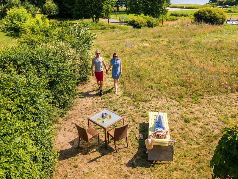 Dos personas caminan por un campo soleado cerca de una mesa y una tumbona con bebidas.