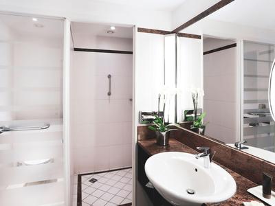 Modern hotel bathroom with white sink, shower, and large mirror.
