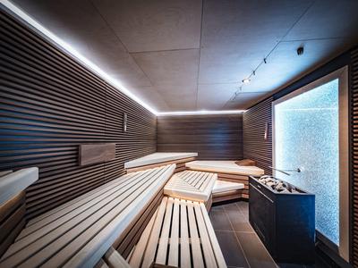 Nowoczesna, stylowo oświetlona sauna z wielopoziomowymi drewnianymi ławkami i piecem do sauny.