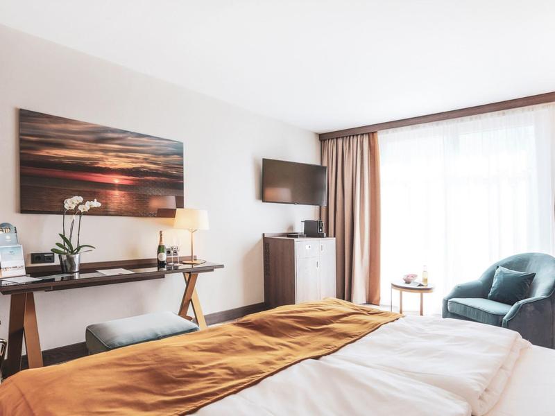 Jasny pokój hotelowy z łóżkiem podwójnym, fotelem, biurkiem i telewizorem