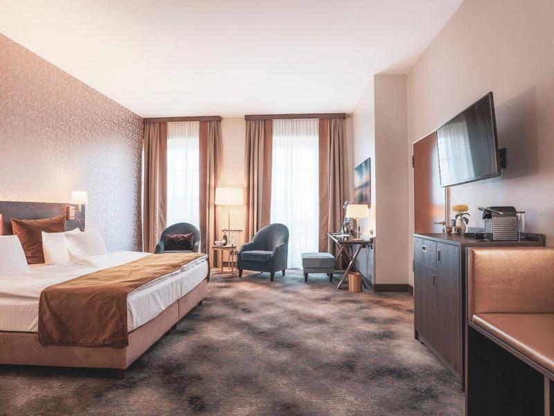 Nowoczesny pokój hotelowy z podwójnym łóżkiem, fotelami, biurkiem i telewizorem z płaskim ekranem.