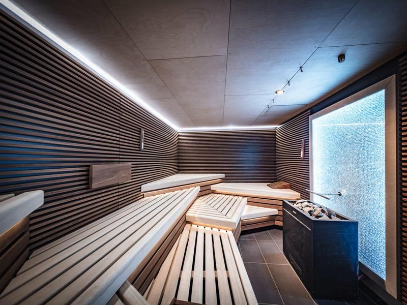 Nowoczesna, stylowo oświetlona sauna z wielopoziomowymi drewnianymi ławkami i piecem do sauny.