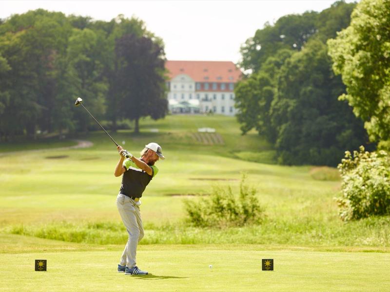 Golfista uderza piłkę na zielonym polu golfowym z zamkiem w tle