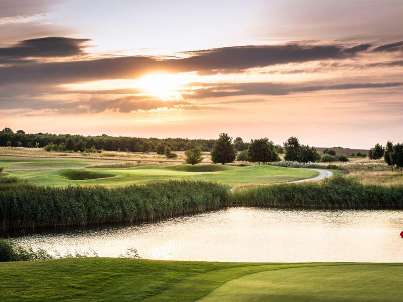 Pole golfowe z oczkiem wodnym i czerwoną chorągiewką o zachodzie słońca