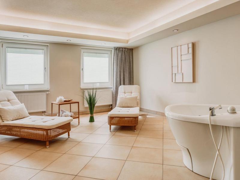 Heller Wellnessraum mit zwei Liegestühlen, Pflanze und rundem Whirlpool.