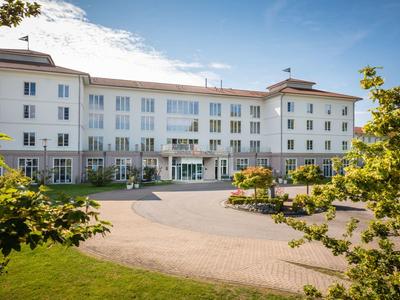 Large white hotel building with many windows, surrounded by trees and a paved driveway.