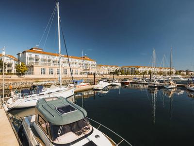 Sailboats and yachts docked in a calm marina in front of a hotel under a clear sky.