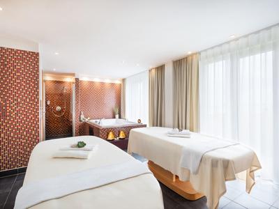 Bright spa room with two massage tables and large windows with curtains.