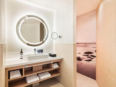 Modern bathroom with illuminated mirror and open shelves next to a shower area featuring a sea view image.