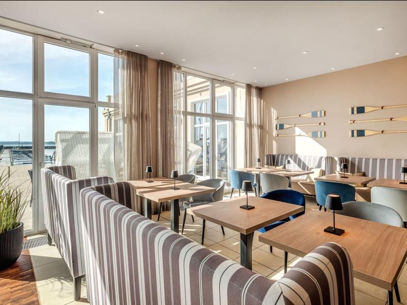 Bright restaurant with large windows, wooden and striped upholstered furniture, and terrace view.