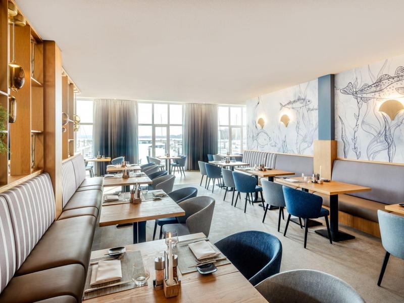 Modern hotel lounge with tables, chairs, illuminated windows, and stylish wall decor.