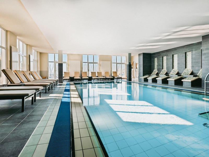 Indoor pool with comfortable lounge chairs and large windows letting in natural light.