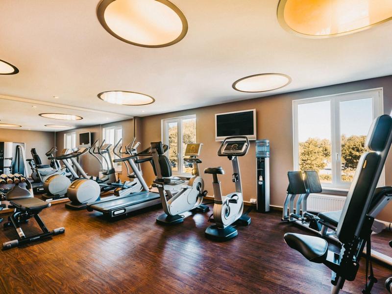 Brightly lit gym with modern equipment and wooden floor in a hotel.