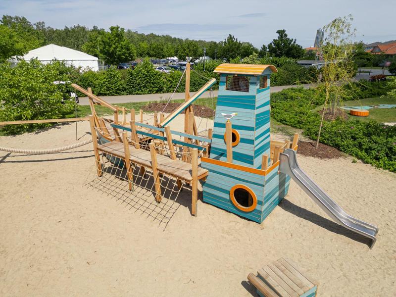 Colorful wooden ship playground with climbing net and slide in sandy area.