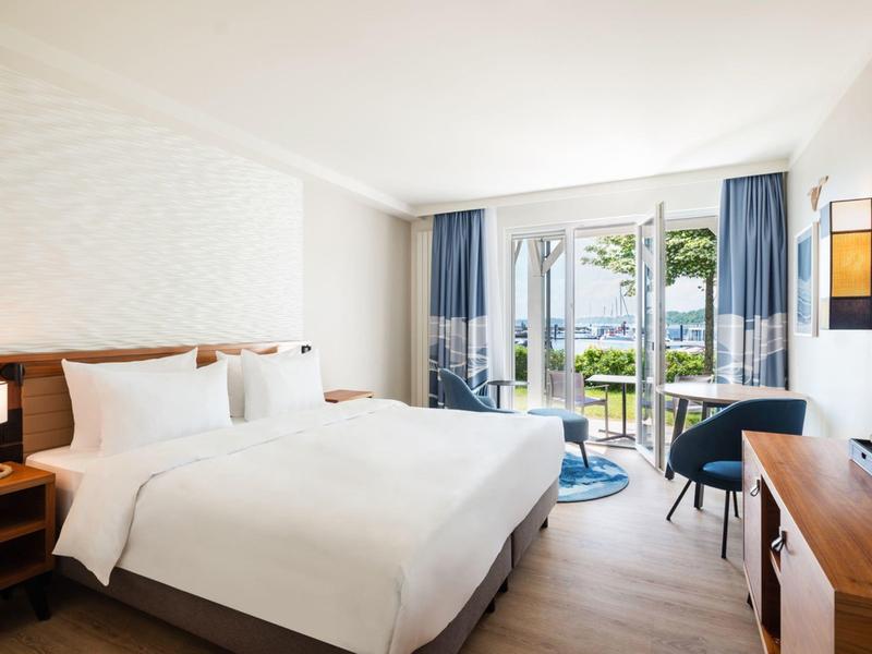 Modern hotel room with double bed, balcony, and sea view.