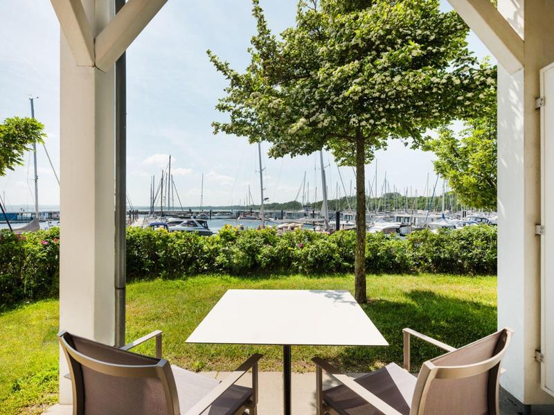 Patio with table and chairs overlooking a marina and green lawn.