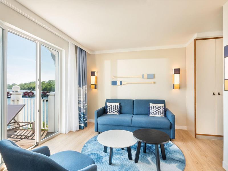 Modern living room with blue sofa, armchair, round rug, and balcony with chairs.