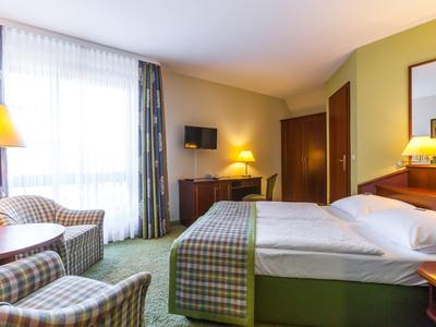 Chambre d'hôtel lumineuse avec lit double, deux fauteuils, bureau et téléviseur.