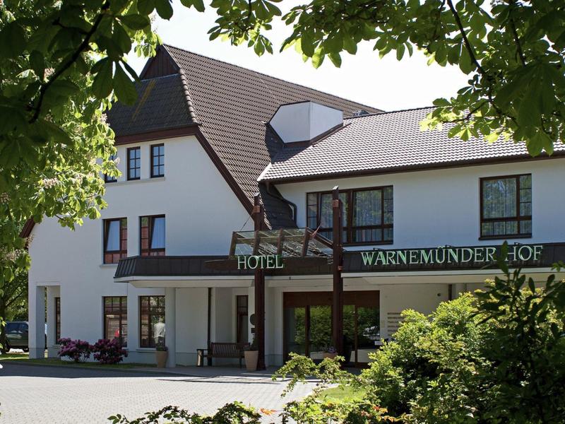 Bâtiment d'hôtel avec toit brun foncé et enseigne verte, entouré d'arbres et d'arbustes.