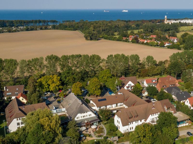 Vue aérienne d'un petit village avec des maisons, des champs et la mer en arrière-plan.