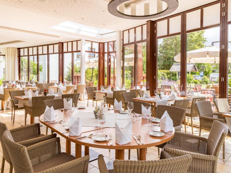 Restaurant lumineux avec tables élégantes, serviettes pliées et grandes fenêtres donnant sur la terrasse.