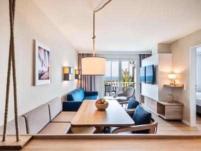 Espace de vie d'hôtel moderne avec coin salon, table à manger, TV et balcon avec vue sur la mer.