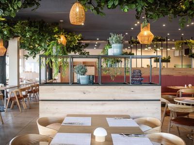 Restaurant moderne avec tables en bois, chaises et plantes vertes suspendues au plafond.