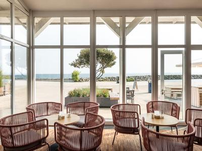 Café moderne avec des chaises en osier et vue sur la plage à travers de grandes fenêtres.