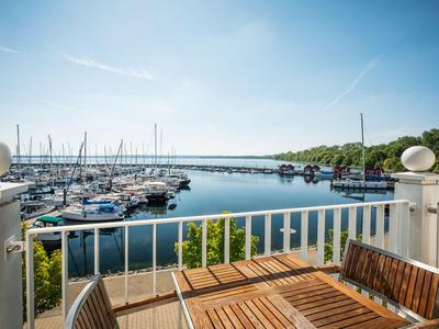 Vue depuis une terrasse avec table et chaises en bois sur une marina avec des voiliers sous un ciel dégagé.