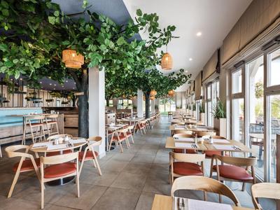 Restaurant moderne avec tables en bois, chaises et plantes vertes suspendues au plafond.