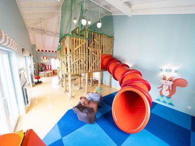 Espace de jeu intérieur avec toboggan rouge, figure d'ours et structure d'escalade pour enfants.