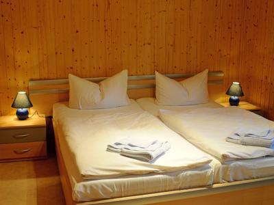 Przytulny pokój hotelowy z dwoma pojedynczymi łóżkami, drewnianymi ścianami i dwoma lampkami nocnymi.