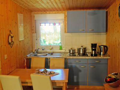 Mała kuchnia z drewnianymi ścianami, niebiesko-białymi szafkami, stołem i dwoma krzesłami.