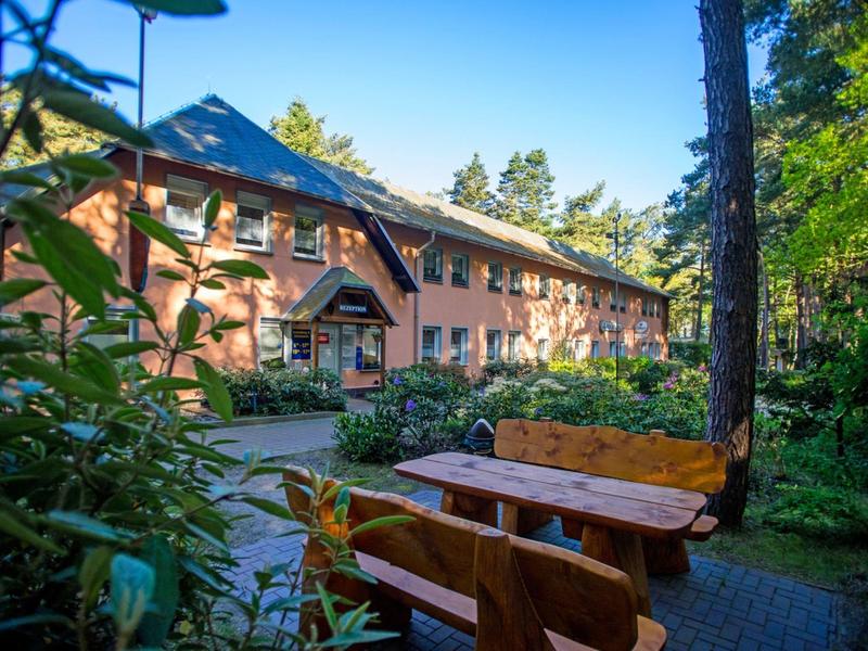 Edificio in mattoni in una foresta verde con panchine e tavoli di legno in primo piano