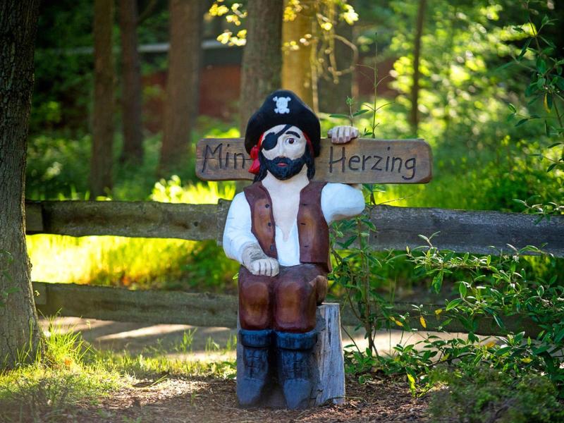 Figura di legno di un uomo con cappello seduto su una sedia nella foresta, accanto a un cartello