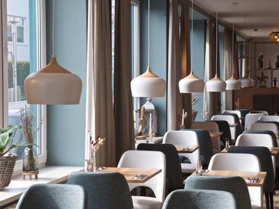 Moderní jídelna s velkými okny a kulatými lampami nad stoly.