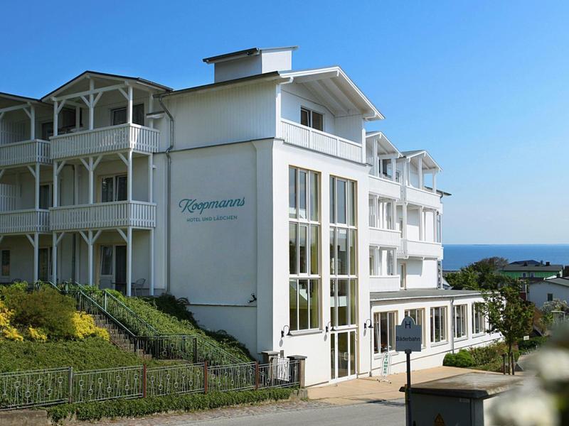 Weißes Hotelgebäude mit großen Fenstern, umgeben von Grün und Blauem Himmel am Meer