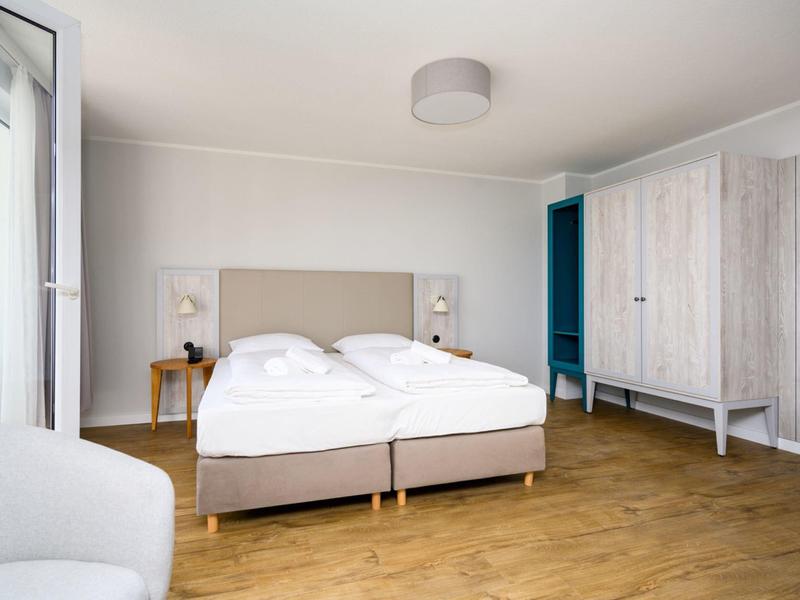 Helles Hotelzimmer mit Doppelbett, weißen Wänden und Holzboden.