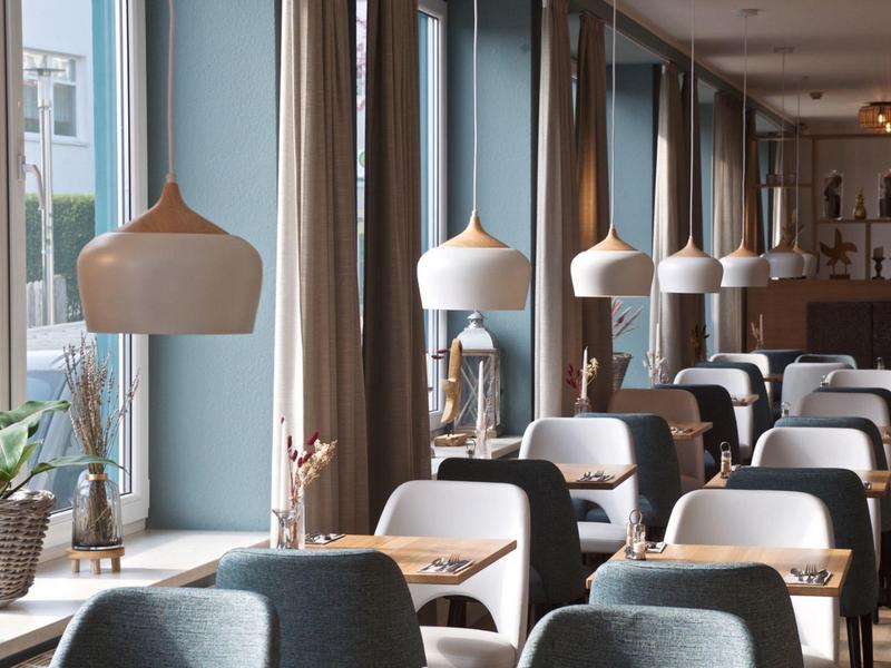 Modernes Restaurant mit grauen Stühlen, Holztischen und großen Hängelampen an Fenstern.