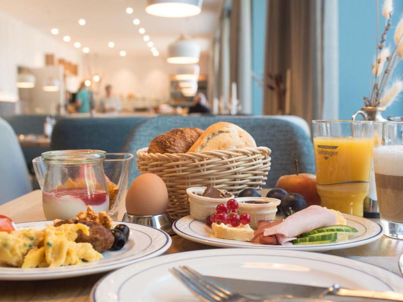 Frühstückstisch mit Eiern, Obst, Brötchen und Orangensaft in einem hellen Restaurant.