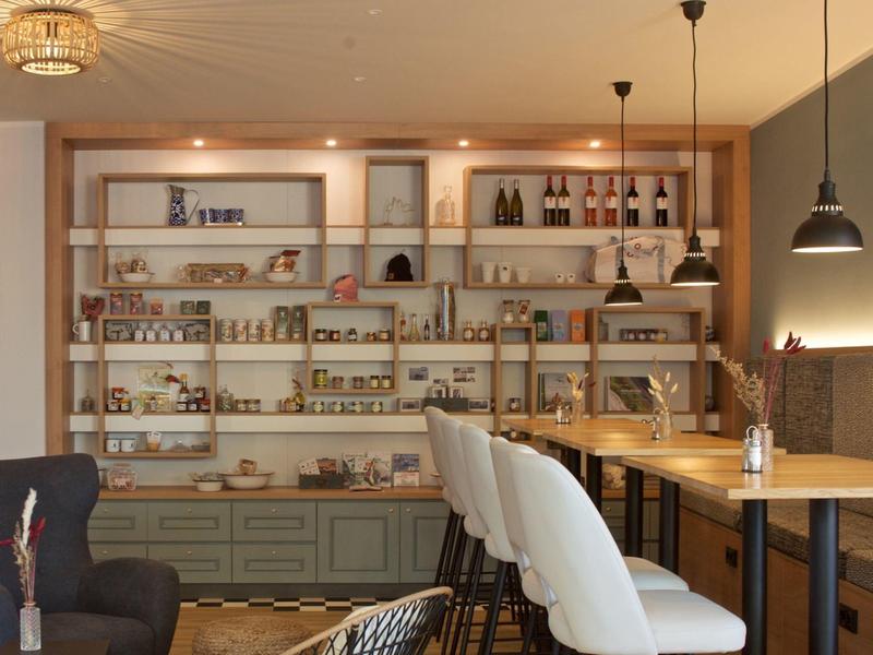 Modernes Café mit Holzregalen voller Produkte und Sitzgelegenheiten mit weißen Stühlen und Holztischen.